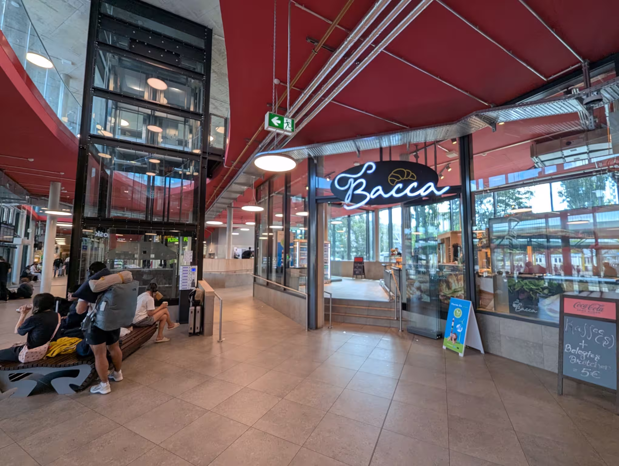 Das Zentrum der Wartehalle mit einem Aufzug links und dem Backwarengeschäft Bacca rechts