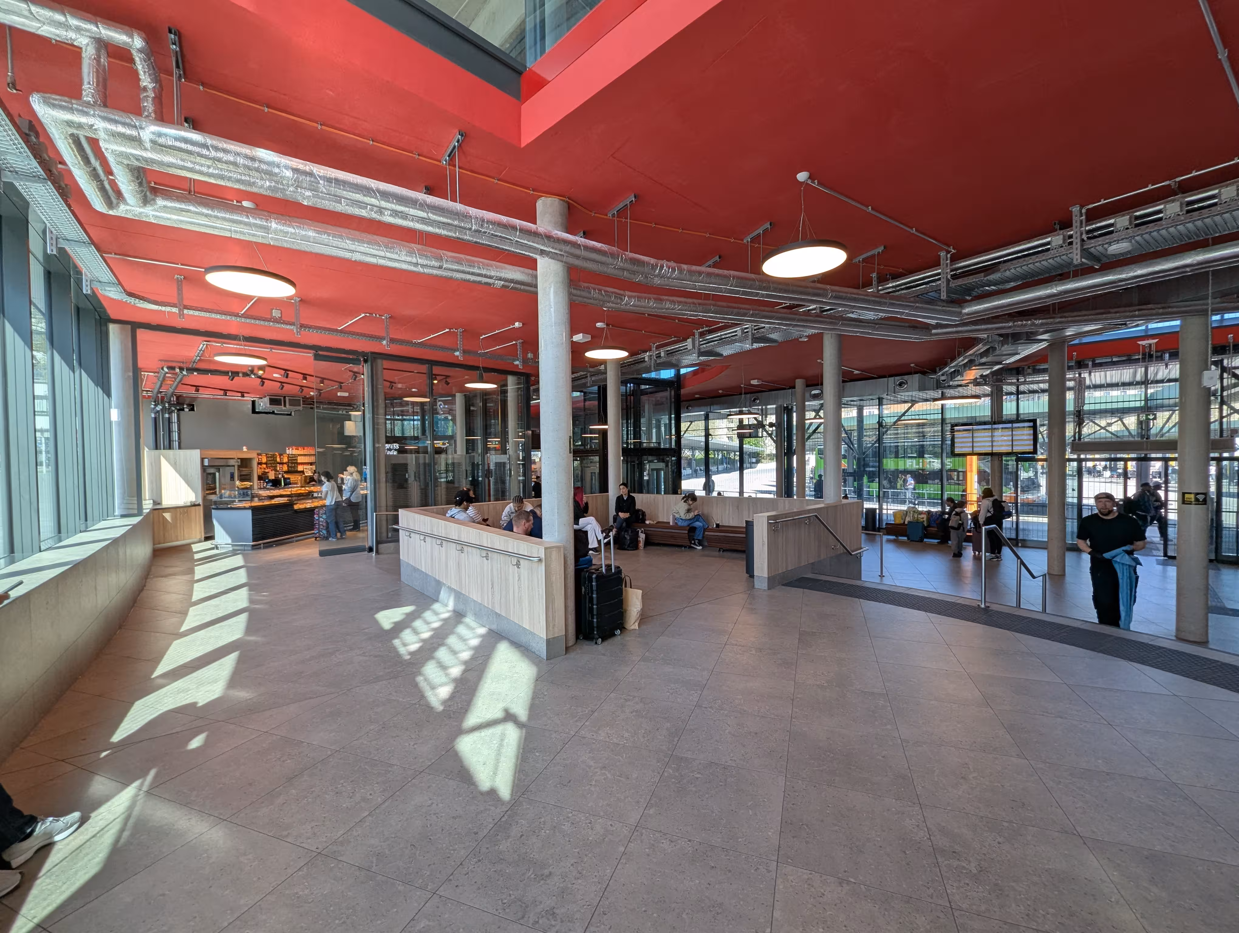 Eine Innenaufnahme der Wartehalle mit einer Sitzecke, Ankunftstafel, und einer Glasfront
