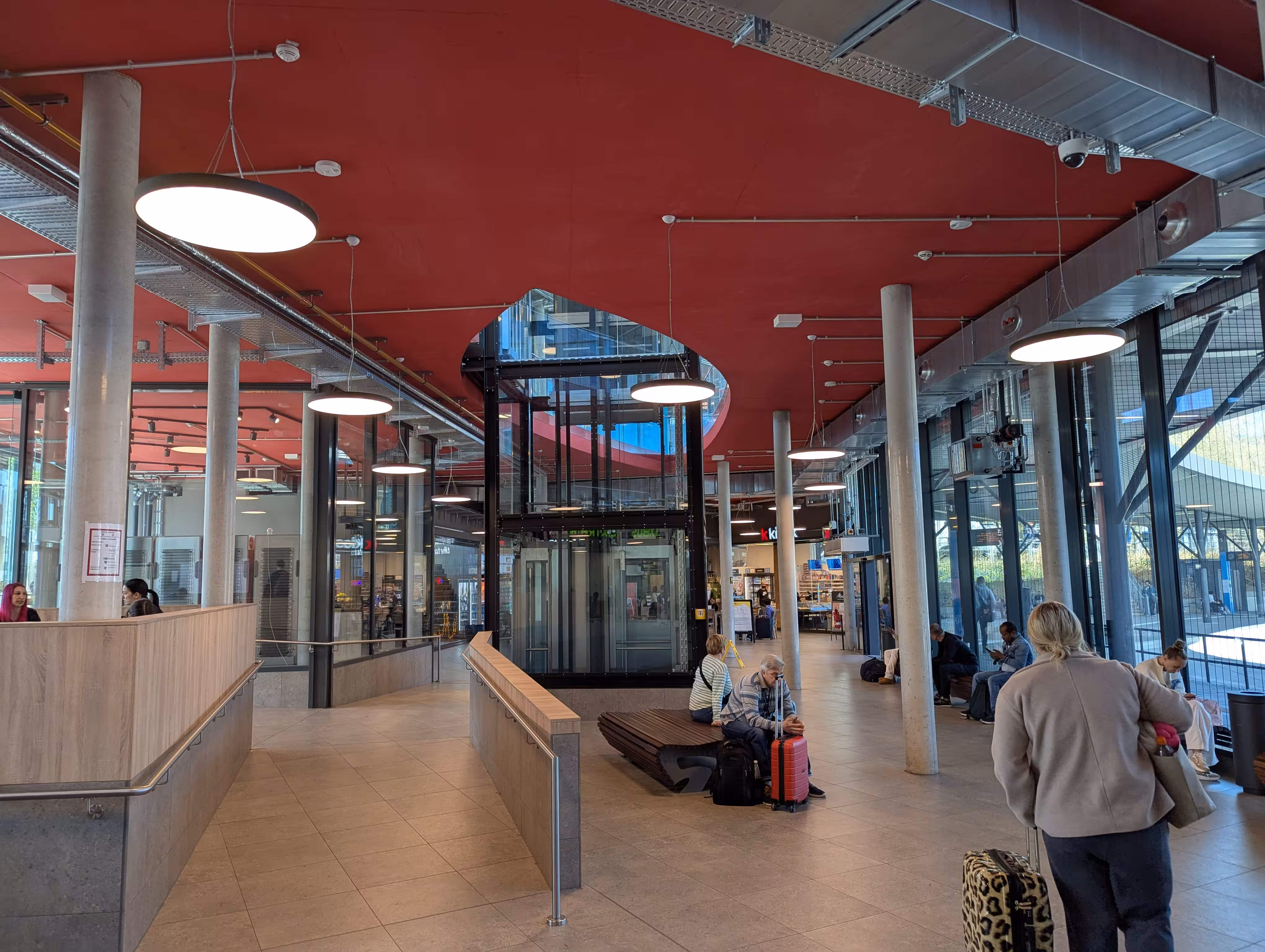 Ein Bild aus dem Zentrum der Wartehalle, im Zentrum befindet sich ein Aufzug, hinter welchem der Gastronomiebereich liegt.