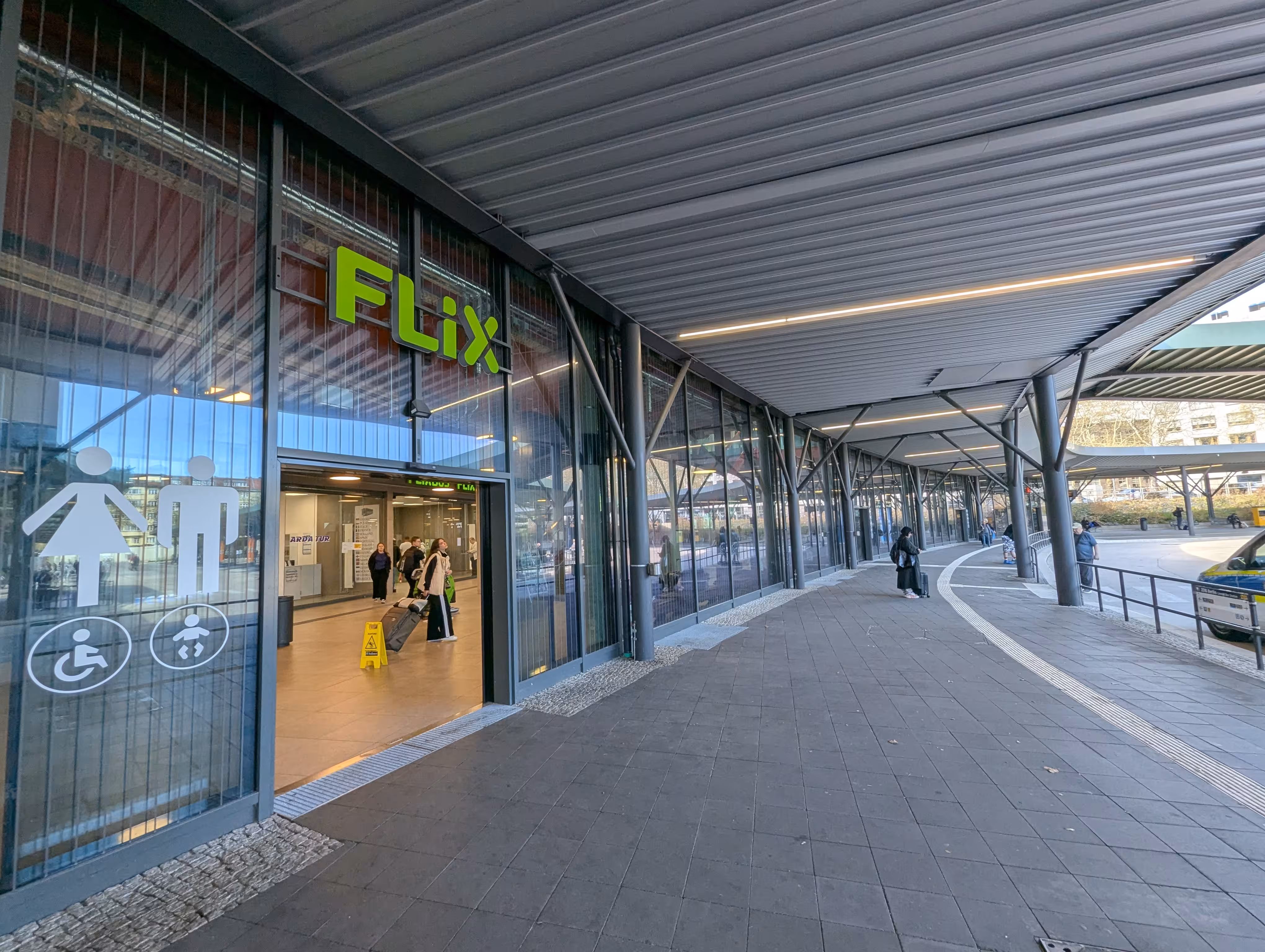 Ein Eingang zur Wartehalle, über ihm hängt ein Flixbus Logo, neben der Tür ist Toilettenbeschilderung angebracht.